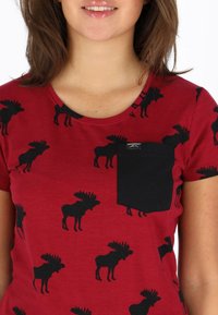 Röd T-shirt med kort ärm och mönster av svarta älgar. Har en svart ficka på vänster bröst och rund halsringning. Mjuk tygtextur.