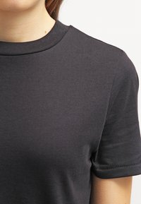 Camiseta negra de manga corta hecha de suave material de algodón. Presenta un cuello redondo y una textura suave con bordes acabados de manera prolija.