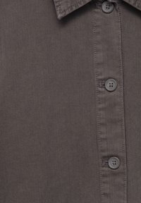 Camicia grigia a spina di pesce con colletto button-down. Caratterizzata da bottoni grigi arrotondati e un tessuto liscio e strutturato.