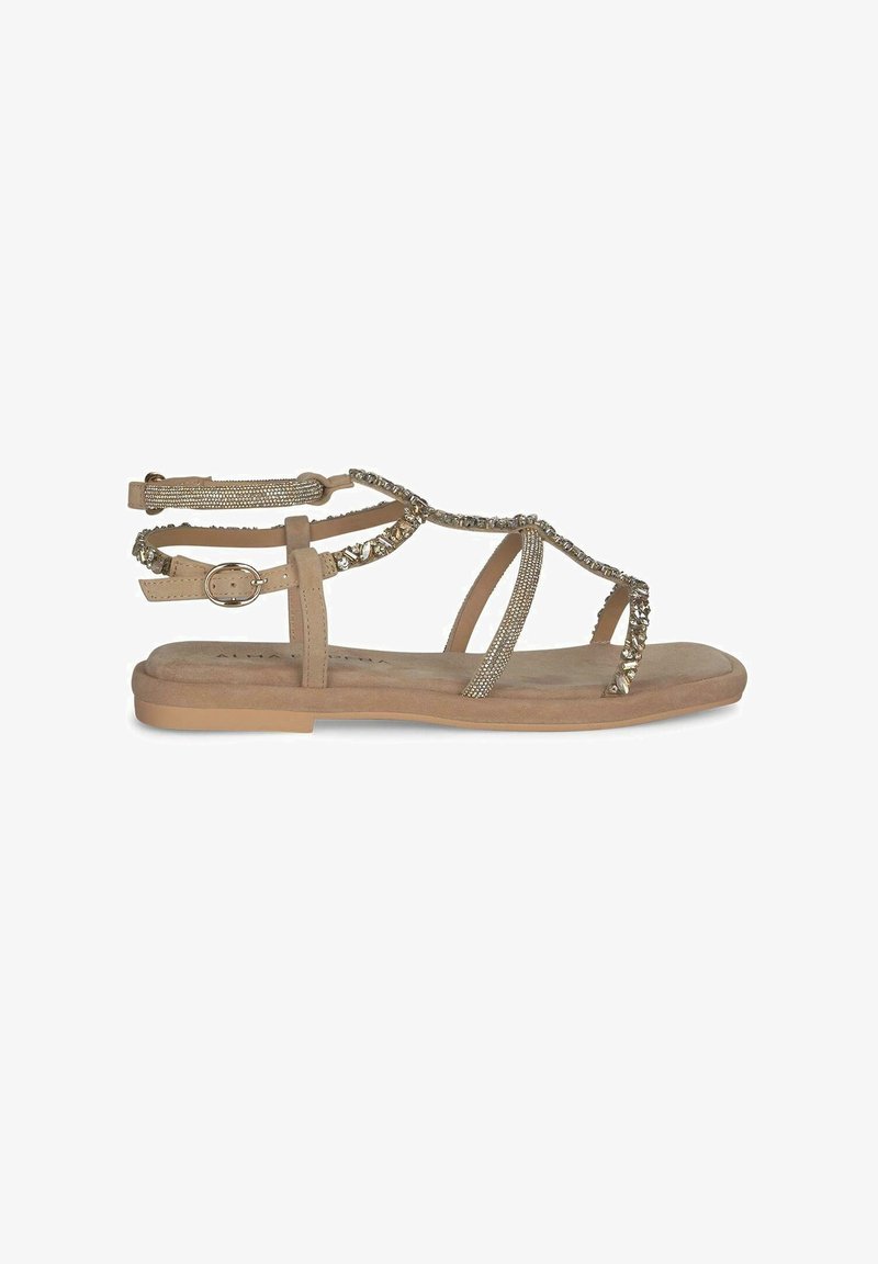 Beżowe płaskie sandały z krzyżującymi się paskami ozdobionymi metalowymi akcentami i cyrkoniami, z regulowanym paskiem na kostkę dla lepszego dopasowania.