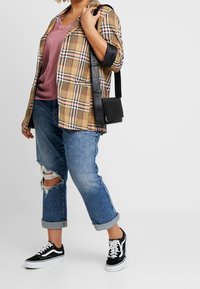 Woman wearing rolled-up ripped blue jeans, black and white sneakers, mauve top, beige plaid blazer, and carrying black shoulder bag.