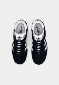 Sorte Adidas Gazelle joggesko med hvite striper og snøringer, sett ovenfra på en hvit bakgrunn.