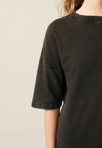 Dark gray oversized t-shirt with short sleeves, ribbed neckline, and visible stitching details, made from a soft, textured fabric.
