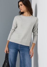 Lichtgrijze trui met ronde hals, gegolfde manchetten en zoom, gecombineerd met blauwe wijdvallende jeans. De textuur is soepel met een zachte uitstraling.