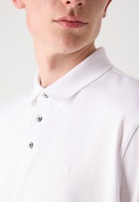 Wit poloshirt van gladde stof, met een platte kraag, vijf knopen en een klein reliëflogo op de borst.