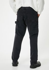 Pantalones cargo negros hechos de una mezcla de algodón, con bolsillos laterales, bolsillos traseros y un ajuste relajado. La tela tiene una textura suave y mate.