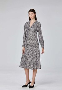 Robe à imprimé floral noir et blanc avec longues manches, décolleté en V et silhouette en A, fabriquée dans un tissu léger. Portée avec des talons noirs.