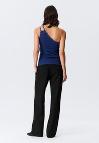 Σκούρο μπλε ριμπ τοπ χωρίς μανίκια με έναν ώμο, διακοσμημένο με ασημένιες τρούκ κατά μήκος του λουριού και εφαρμοστή γραμμή. Συνδυασμένο με μαύρο παντελόνι.