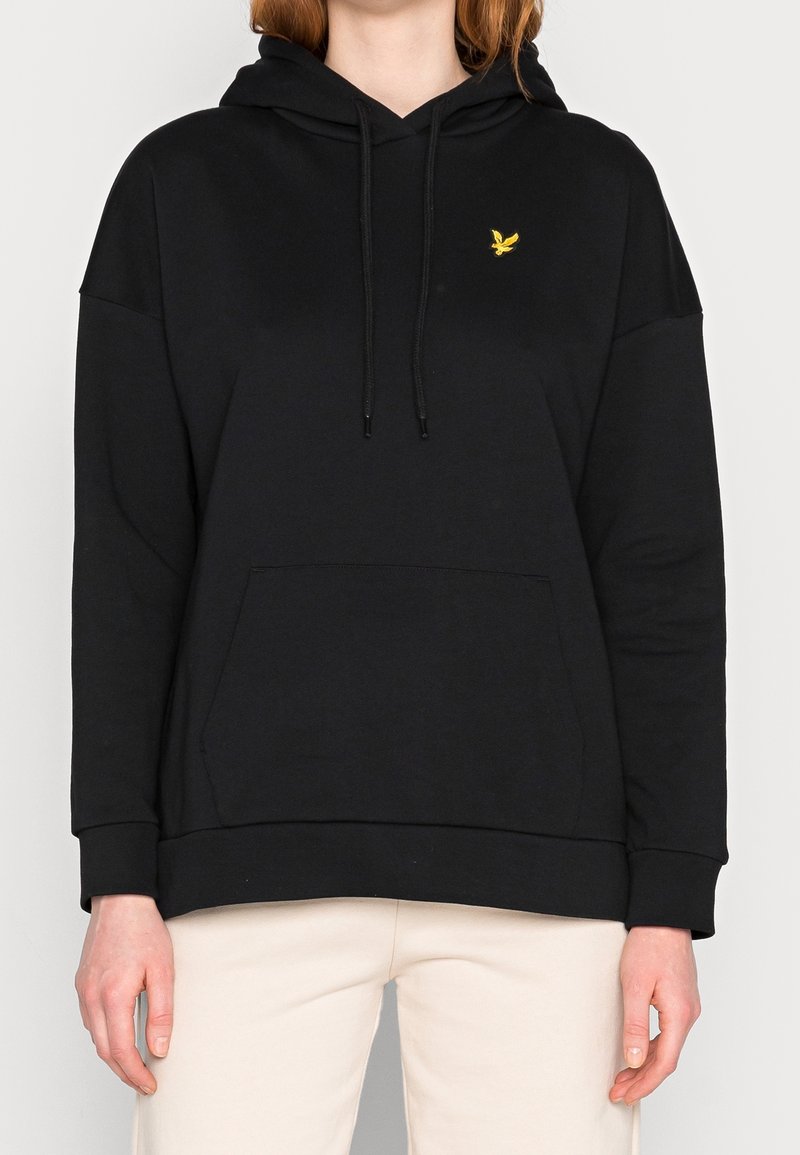 Haut à capuche noir en coton avec une poche avant, cordon de serrage et un petit logo d'oiseau jaune sur le côté gauche de la poitrine. Texture douce, design décontracté.