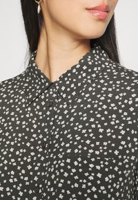 Chemise vert foncé avec un motif floral comportant de petites fleurs blanches, col classique, fermeture à boutons sur le devant et texture subtile.