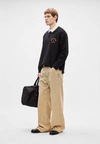 Μαύρο μακρυμάνικο πόλο μπλουζάκι με κόκκινο λογότυπο, μπεζ παντελόνι σε φαρδιά γραμμή και μαύρη τσάντα. Λείος ύφασμα, αντίθετα υφάσματα, κομψός σχεδιασμός.