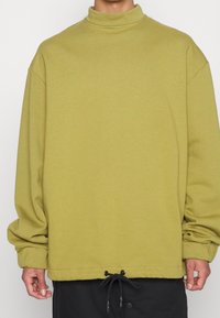 Pullover verde con collo alto, maniche lunghe e orlo con cordoncino. Realizzato in materiale morbido, presenta una vestibilità comoda.