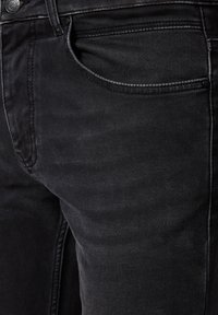 Zbliżenie czarnych dżinsów z denimu, ukazujące szczegóły przedniej kieszeni, guzika i przeszyć na teksturowanej tkaninie.