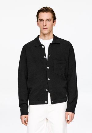 Black cardigan made of textured material with a collared neck, front buttons, a patch pocket, and ribbed cuffs and hem.