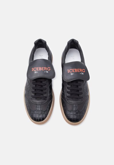 Paire de baskets noires avec motif texturé, lacets noirs, semelles beiges, et languette noire portant l'inscription "ICEBERG 1974" en texte rouge.