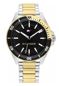 Tommy Hilfiger-klocka med en svart urtavla, band av rostfritt stål i silver och guldton, tydliga timmarkeringar och en ensidig bezel.