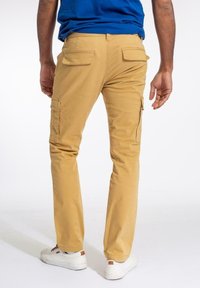 Khaki cargo kalhoty rovného střihu, s dvěma zadními kapsami a bočními kapsami, vyrobené z bavlněné látky. Nosené s bílými teniskami.