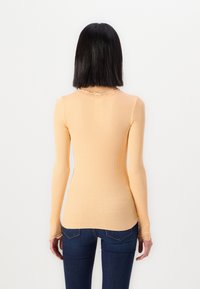 Geribbelde langslavige top in zacht perzik met een ronde halslijn met kant en een getailleerd silhouet, gecombineerd met donkerblauwe jeans.