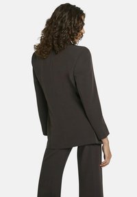 Donkerbruine op maat gemaakte blazer met een enkele split, gestructureerde schouders en lange mouwen, gecombineerd met bijpassende op maat gemaakte broeken.