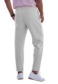 Graue Jogginghosen mit elastischem Bund, zwei Gesäßtaschen, schmal zulaufenden Beinen und Bündchen; kombiniert mit weißen Sneakers. Texturiertes Baumwollgemisch.