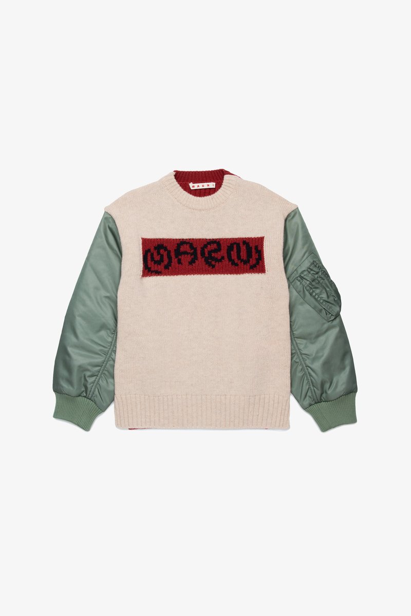 Sweater with a cream knitted body, green satin sleeves, maroon ribbed collar, and a red knitted logo panel with black design. Textured and structured.