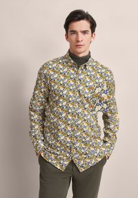 Langarmhemd mit floralem Muster, das orangefarbene, lila und grüne Blumen auf weißem Hintergrund zeigt, mit Button-Down-Kragen und Brusttasche.