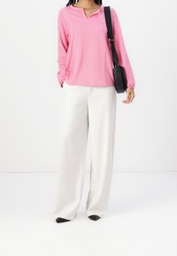 Vaaleanpunaiset raidalliset pitkät hihansuut V-pääntiellä, yhdistettyinä leveälahkeisiin valkoisiin housuihin. Ilmettä täydentää musta olkalaukku.