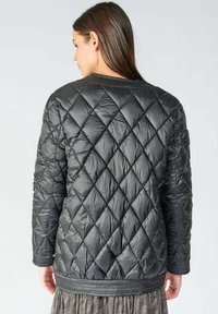 Veste matelassée noire avec un motif en losanges, tissu texturé, poignets côtelés et ceinture. Le design est léger et moderne.