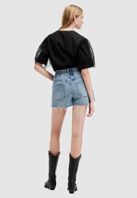 Top negro de manga abullonada con lunares, shorts de mezclilla desgastados y botas vaqueras negras hasta la rodilla. El conjunto muestra una variedad de texturas y estilos.