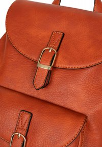 Bruine leren rugzak met een ronde klep en een gouden gesp, gestructureerd oppervlak, contrasterende stiksels en een slank ontwerp.