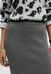 Jupe grise en tricot avec une texture lisse et une taille ajustée, associée à un pull noir et gris à motifs.