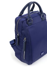 Kompakt marinblå ryggsäck med dubbla handtag upptill, framficka med dragkedja, silverfärgad dragkedjor och slät tygstruktur på vit bakgrund.