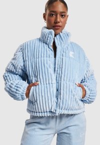Veste doudoune en peluche côtelée bleu clair avec un col haut, une fermeture éclair et des poignets élastiques. Comprend des poches latérales et un logo brodé.