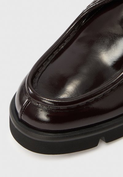 Tamsiai burgundiškos spalvos odiniai batai su blizgiu paviršiumi, apvaliu nosimi ir storu juodu guminės padų. Viršuje matomos subtilios siūlės.