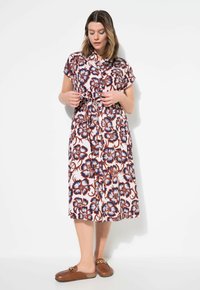 Vestido con estampado floral en tonos rosa, azul y marrón, con mangas cortas, cintura anudada y silueta fluida, combinado con zapatos marrones de slip-on.