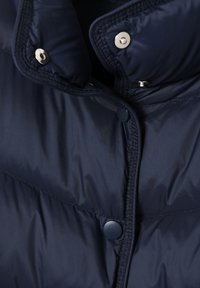 Gros plan sur une veste matelassée bleu marine avec un col rembourré et des boutons-pression de tailles différentes pour fermer le devant.