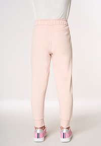 Joggers rosa chiaro realizzati in tessuto morbido, con vita elastica, gambe affusolate e una piccola tasca posteriore. Abbinati a sneaker rosa.