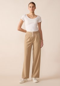 Witte, aansluitende t-shirt gecombineerd met hoogwolde, losse beige broeken met zijplooien, een aangesnoerde tailleband en witte sneakers.