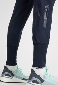 Marineblauwe sportbroeken met zwarte glanzende accenten aan de zijkanten, gecombineerd met grijze en muntgroene hardloopschoenen en witte sokken.