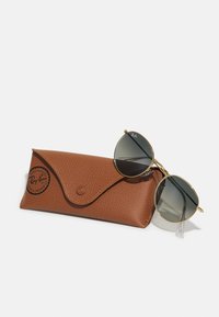 Occhiali da sole Ray-Ban con lenti scure rotonde e montatura in metallo dorato, appoggiati in un astuccio in pelle marrone texturizzata con chiusura a scatto e logo.