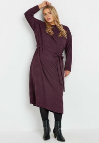 Lila, ribbad långärmad klänning med knytbältet i midjan, i midi-längd och med sidofålla. Bärs med svarta ankelstövlar.