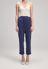 Body crema a costine con scollatura a V, abbinato a pantaloni navy sartoriali con vita a cordoncino e maniche arrotolate, indossato con scarpe bianche con tacco.