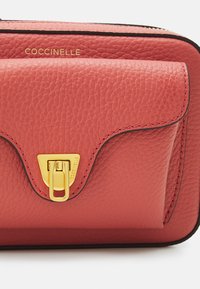 Borsa in pelle rossa con texture, chiusura a patta, hardware color oro, logo prominente e bordi a contrasto. Forma compatta e rettangolare.