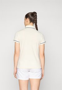 Kortärmad polo t-shirt i ljus beige, med marinblå accentfärger på krage och ärmslut. Slät bomullsmaterial och figursydd design.
