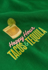 Tissu vert avec texte brodé « Happy Hour TACOS & TEQUILA » et un dessin d'un verre de tequila avec un quartier de citron vert.