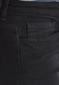 Zwarte denim jeans met een slim fit, voorzien van een achterzak en subtiele stikdetails. De stof heeft een gladde, zachte textuur.