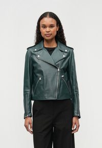 Zelena usnjena motoristična jakna s srebrno strojno opremo, asimetričnim zadrževalnim zaprtjem in dvema stranskima žepoma z zadrgo. Strukturiran kroj z ovratnikom reverjem.