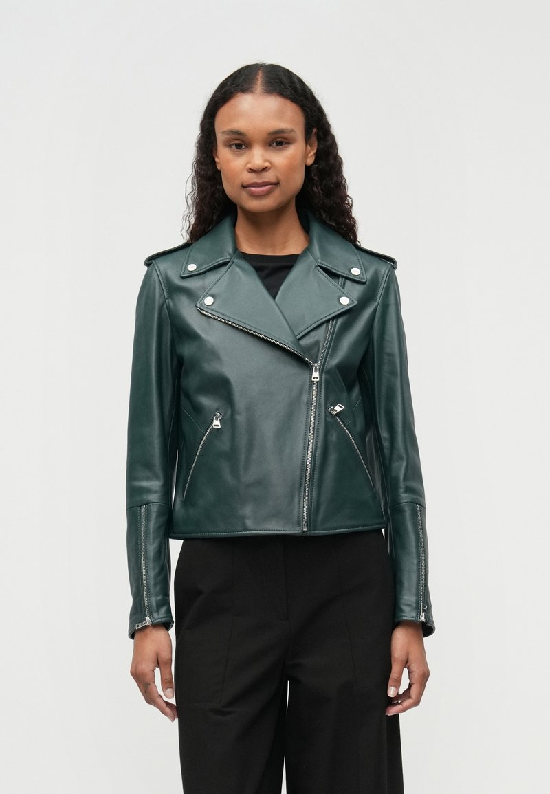 Zelena usnjena motoristična jakna s srebrno strojno opremo, asimetričnim zadrževalnim zaprtjem in dvema stranskima žepoma z zadrgo. Strukturiran kroj z ovratnikom reverjem.