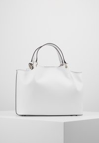 Sac à main blanc avec une texture lisse, accents noirs le long des bords, doubles anses supérieures et détails en métal.