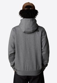 Felpa grigia con una texture accogliente, dotata di cappuccio e polsini a coste. Presenta un piccolo logo nero sulla parte superiore della schiena.